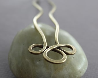 May include: A brass hair pin with a simple, elegant design. The pin is shaped like a figure eight and has a smooth, polished finish.