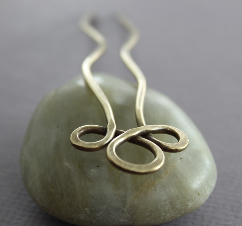 May include: A brass hair pin with a simple, elegant design. The pin is shaped like a figure eight and has a smooth, polished finish.