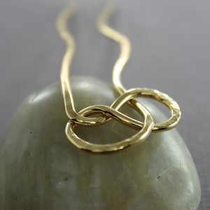 May include: A gold necklace with a hammered, knotted design. The necklace is made of a single piece of wire that is twisted and knotted to create a unique and modern look.