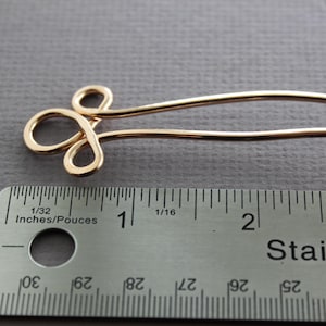 May include: Gold-toned metal hair pin with a decorative loop design. The pin is approximately 1 inch long and is measured against a ruler.