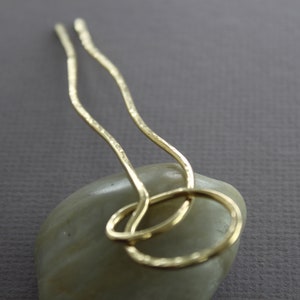 May include: Two gold hair pins with a textured finish, twisted together in a circle shape.