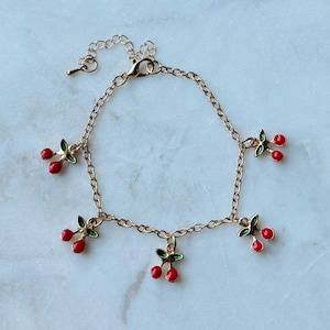 May include: A gold chain bracelet with five dangling charms shaped like red cherries with green leaves.