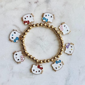 May include: A gold charm bracelet with multiple white Hello Kitty charms with colorful bows. The charms are attached to a gold chain bracelet.