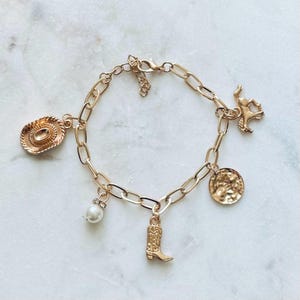 May include: Gold charm bracelet with a cowboy hat, boot, horse, pearl, and a textured coin charm.