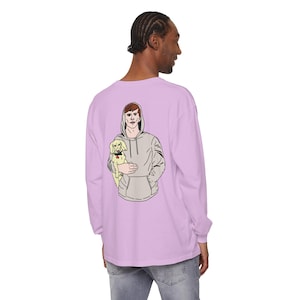 May include: A lavender long-sleeve t-shirt with a graphic print of a man in a grey hoodie holding a small dog. The man has red hair and the dog is white.