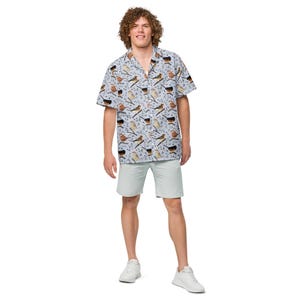 May include: A short-sleeved button-down shirt featuring a repeating pattern of various small birds perched on branches against a light blue background, paired with light gray shorts and white sneakers.