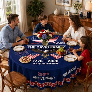 May include: A round navy blue tablecloth with a patriotic design. The tablecloth features the text "250th Anniversary" and "1776-2026 Semicentennial". An American flag and an eagle are also featured in the design. The tablecloth is set on a wooden table.
