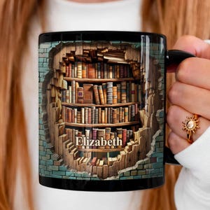 Può includere: Tazza da caffè nera con un'illustrazione dettagliata di una libreria all'interno di un muro. La libreria è piena di vari libri. Il nome "Elizabeth" è stampato sulla tazza. La tazza è tenuta da una persona.