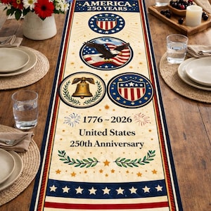 May include: A rectangular table runner with a patriotic theme. It features the text "AMERICA 250 YEARS" and "1776-2026 United States 250th Anniversary." The design includes an eagle, the Liberty Bell, and the American flag.