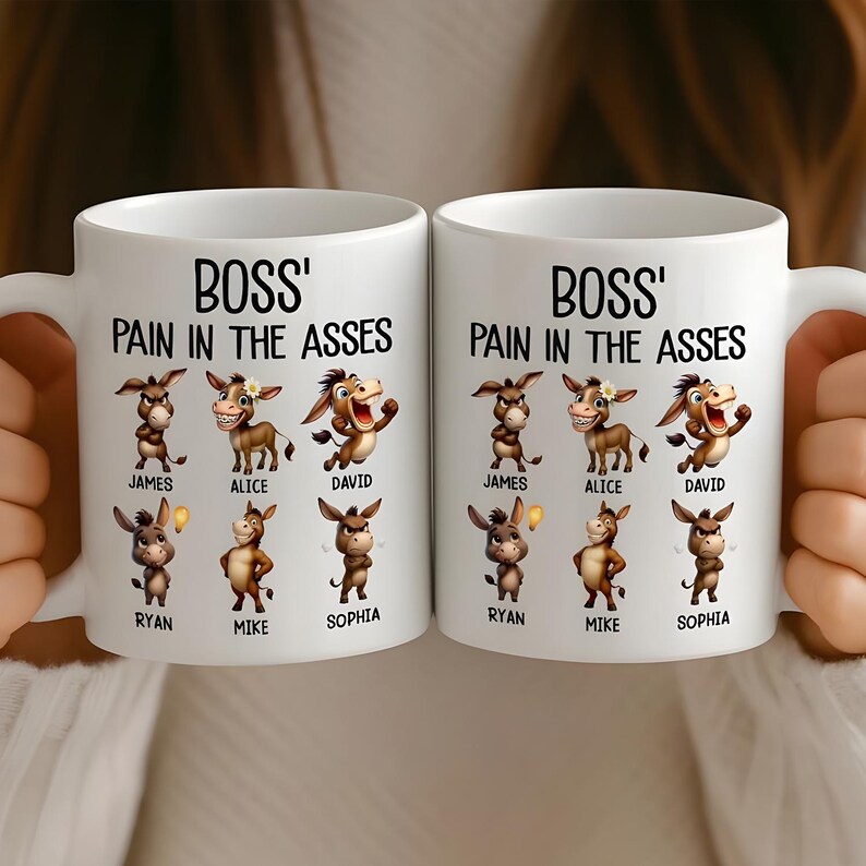 May include: Two white ceramic mugs with the text "BOSS' PAIN IN THE ASSES" and cartoon donkeys. Each mug features names like James, Alice, David, Ryan, Mike, and Sophia. The mugs are held by a person.