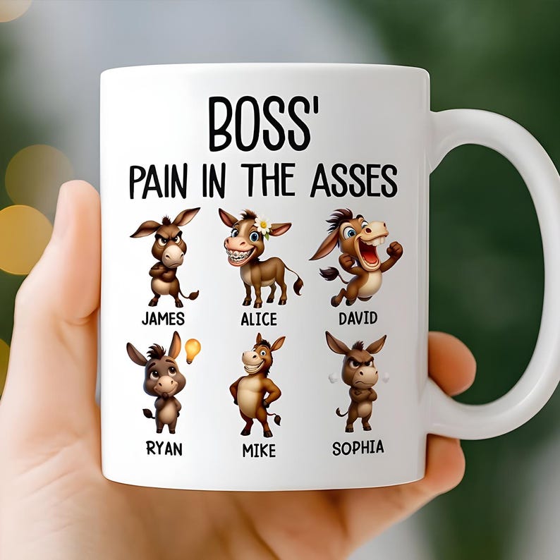 May include: White ceramic mug with the text "BOSS' PAIN IN THE ASSES" in black. The mug features cartoon donkeys with names like James, Alice, and David. The mug is held by a person.