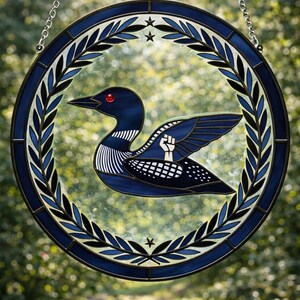 May include: Circular stained glass panel depicting a blue loon with a red eye and a raised fist on its wing. The loon is set within a blue and black circular frame with a laurel wreath and stars. A silver chain is attached for hanging.