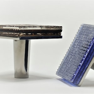 May include: Two stamps with stainless steel handles. One stamp has a rectangular, textured brown surface. The other stamp has a blue, ridged surface. Both stamps are on a white background.
