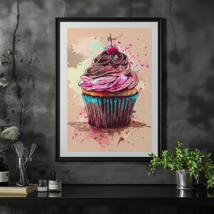 May include: A framed print of a colourful cupcake with pink and brown icing, a red cherry on top, and blue sprinkles. The cupcake is on a light brown background with watercolour splatters.