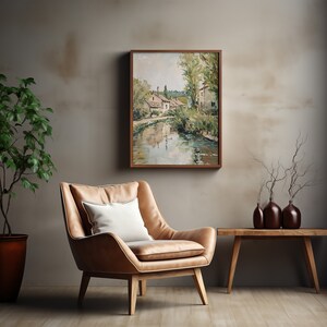 May include: A brown leather armchair with a white pillow sits in front of a framed painting of a village by a river. A wooden table with three brown vases and a dried branch arrangement sits to the right of the chair.