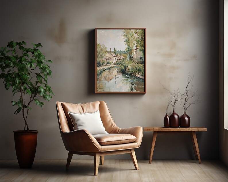 May include: A brown leather armchair with a white pillow sits in front of a framed painting of a village by a river. A wooden table with three brown vases and a dried branch arrangement sits to the right of the chair.