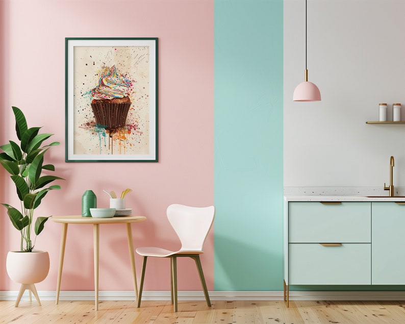 May include: A framed print of a watercolour painting of a cupcake with colourful frosting and sprinkles. The cupcake is on a white background with splatters of paint in various colours. The frame is dark green and the print is hanging on a pink wall.