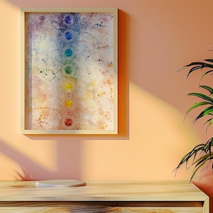 May include: A framed watercolor painting of a chakra system with seven colored circles representing the seven chakras. The painting is on a light peach wall with a potted succulent plant and a wooden table in the foreground.
