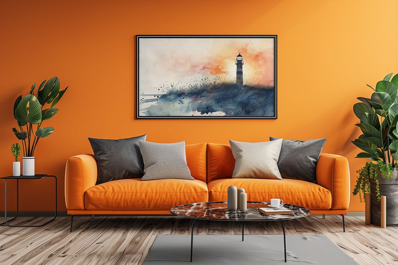 Puede incluir: Una pintura de acuarela de un faro en una playa al atardecer, colgada sobre un sof&aacute; naranja con almohadas en un ambiente de sala de estar.