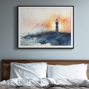 Puede incluir: Una pintura de acuarela de un faro en una costa rocosa con una puesta de sol en el fondo. La pintura est&aacute; enmarcada en negro y colgada en una pared azul claro sobre una cama con ropa de cama blanca.