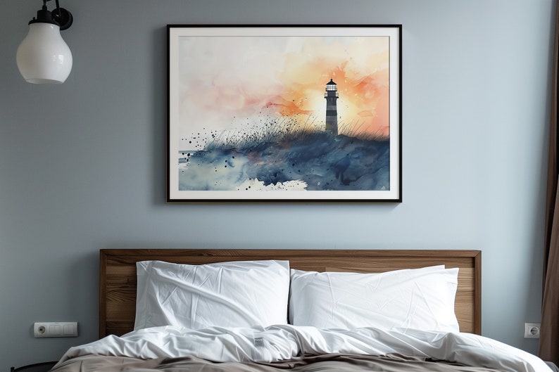 Puede incluir: Una pintura de acuarela de un faro en una costa rocosa con una puesta de sol en el fondo. La pintura est&aacute; enmarcada en negro y colgada en una pared azul claro sobre una cama con ropa de cama blanca.