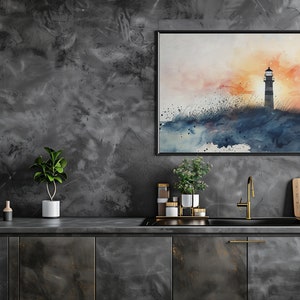 Puede incluir: Una pintura de acuarela de un faro en una costa rocosa con una puesta de sol en el fondo. La pintura est&aacute; enmarcada en negro y colgada en una pared gris en una cocina.