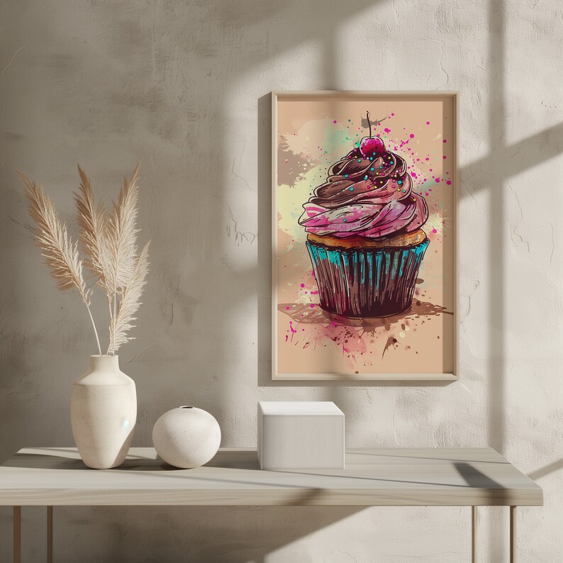 May include: A framed watercolour painting of a pink and brown cupcake with a red cherry on top. The cupcake is decorated with colourful sprinkles and is sitting on a light brown background with watercolour splatters.