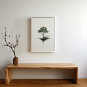 May include: A white framed print of a watercolor painting of a tree growing out of a small island. The island is surrounded by water and the tree has green leaves. The print is hanging on a white wall above a wooden bench.