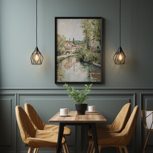 May include: A dining room with a wooden table and four chairs. The table has a black metal frame and a light wood top. The chairs are upholstered in a light brown fabric. A framed painting of a river scene hangs on the wall behind the table. Two black pendant lights hang above the table.