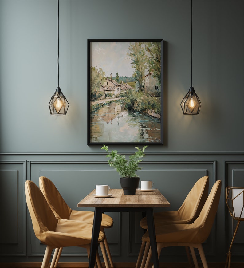 May include: A dining room with a wooden table and four chairs. The table has a black metal frame and a light wood top. The chairs are upholstered in a light brown fabric. A framed painting of a river scene hangs on the wall behind the table. Two black pendant lights hang above the table.