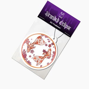 May include: Round air freshener featuring two koi fish in shades of orange and white, surrounded by pink cherry blossoms. The air freshener is packaged with a purple header that reads "Branded Eclipse" and "Air Freshener".
