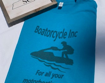 May include: A turquoise blue t-shirt with a dark green graphic of a jet ski and the text "Boatorcycle Inc. For all your motorboating needs."