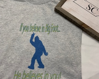 May include: A gray t-shirt with a blue silhouette of Bigfoot and the text "If you believe in Bigfoot... He believes in you!"