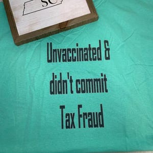 May include: A turquoise blue t-shirt with the text "Unvaccinated & didn't commit Tax Fraud" printed in black.