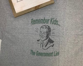 May include: Gray t-shirt with a vintage-style illustration of a man and the text "Remember Kids... The Government Lies."