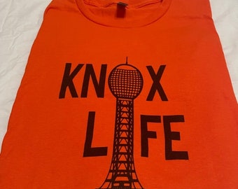 May include: Orange t-shirt with a black graphic of a tower and the text "KNOX LIFE".