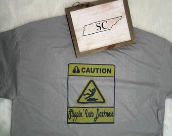 May include: A gray t-shirt with a yellow and black caution sign that reads "Caution Slippin' Into Darkness." A wooden sign with the letters "SC" and the outline of Tennessee is on top of the shirt.