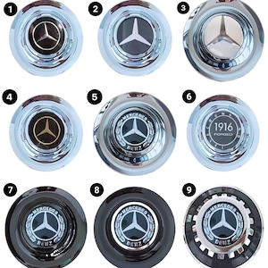 May include: Nine different styles of Mercedes-Benz car emblems. The emblems are silver, black, and gold with a three-pointed star logo. Some emblems have the text "Mercedes-Benz" and "Benz" written on them.