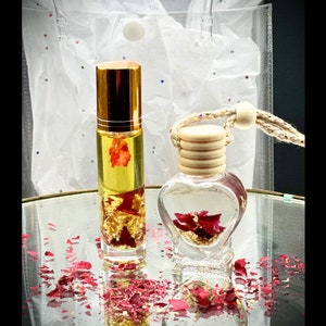 May include: Two glass bottles with gold flakes and red rose petals inside. The bottle on the left is a roller bottle with a gold cap. The bottle on the right is a heart-shaped bottle with a wooden cap and a string.