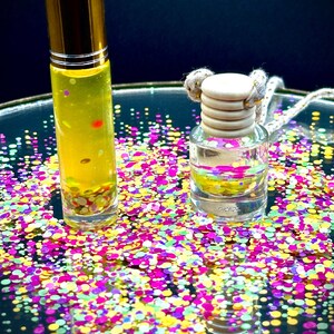 May include: Two glass bottles with gold lids and yellow liquid inside. The bottles are sitting on a surface covered in colorful confetti.