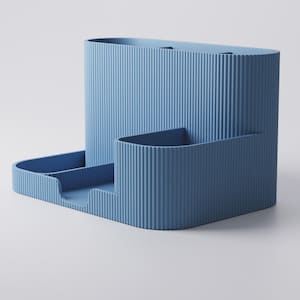 May include: A light blue desk tidy with a ribbed texture. It features a tall, oval-shaped section, a smaller rectangular section, and a tray with two compartments. The design is modern and minimalist.