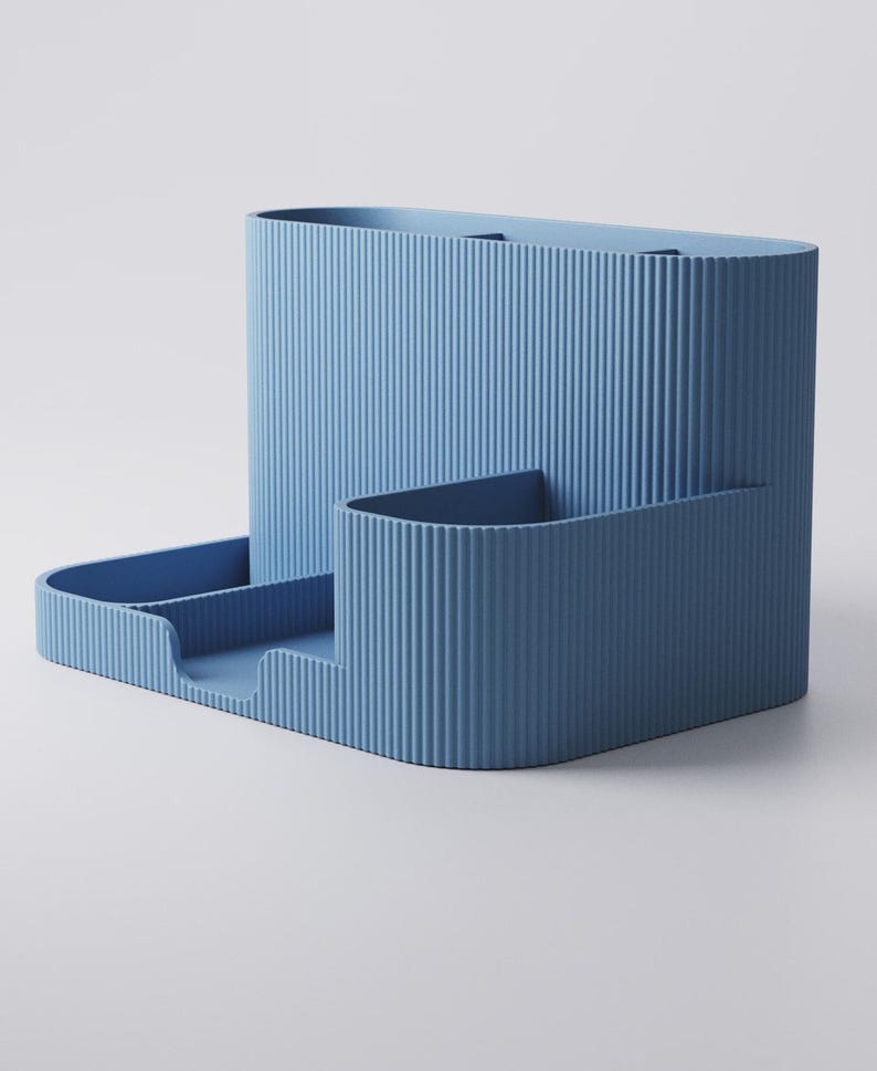 May include: A light blue desk tidy with a ribbed texture. It features a tall, oval-shaped section, a smaller rectangular section, and a tray with two compartments. The design is modern and minimalist.