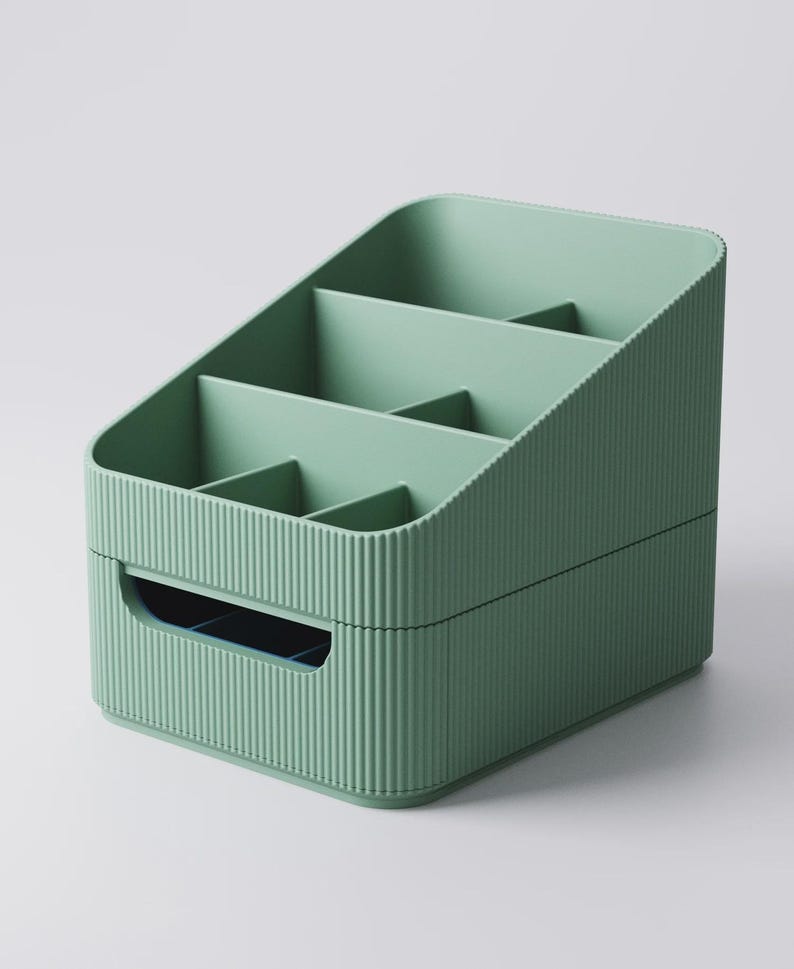 May include: A sage green organizer with multiple compartments. The organizer has a ribbed texture on the exterior and a handle on the front. The interior is divided into several sections, ideal for storing small items. The design is simple and functional.