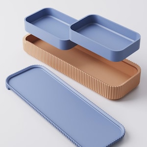 Puede incluir: Un juego de tres bandejas rectangulares en tonos azules y beige. La bandeja m&aacute;s grande es azul con un borde texturizado. La bandeja del medio es beige con estr&iacute;as verticales. Dos bandejas azules m&aacute;s peque&ntilde;as est&aacute;n apiladas encima.