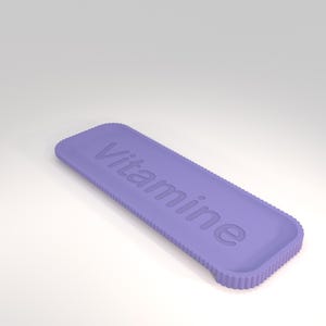 Puede incluir: Un objeto rectangular de color lavanda con la palabra "Vitamine" en relieve en su superficie. Los bordes tienen una textura estriada. El objeto est&aacute; sobre un fondo blanco.