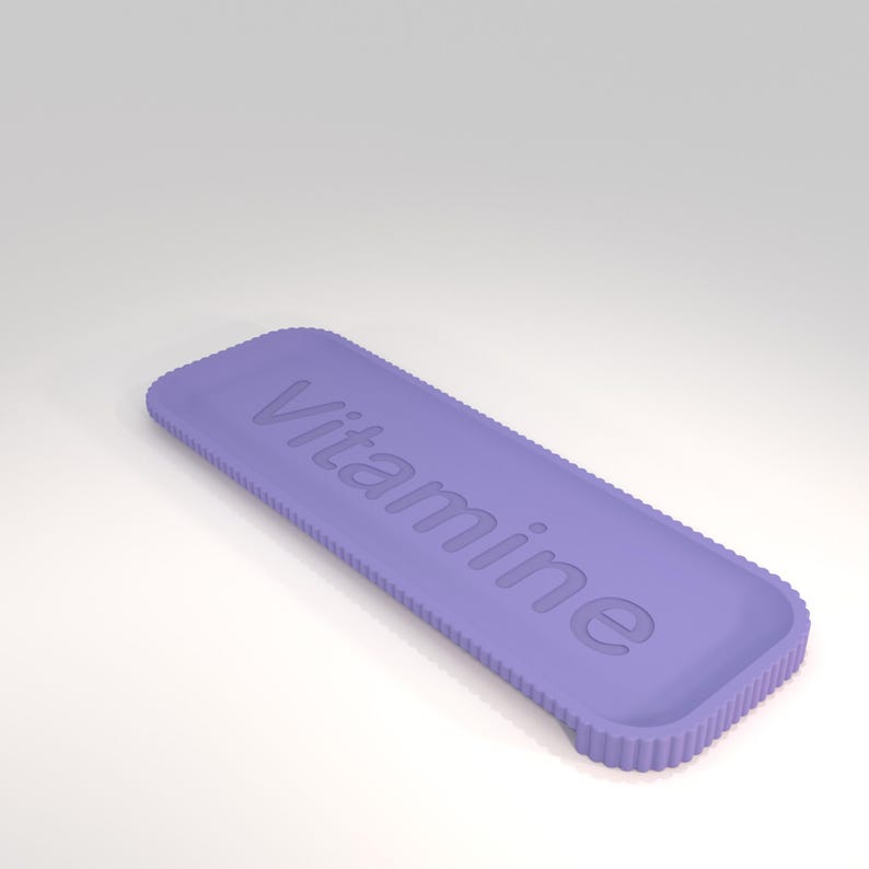 Puede incluir: Un objeto rectangular de color lavanda con la palabra "Vitamine" en relieve en su superficie. Los bordes tienen una textura estriada. El objeto est&aacute; sobre un fondo blanco.