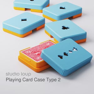 Könnte beinhalten: Eine Sammlung blauer und orangefarbener Spielkartenetuis mit Aussparungen für Spielkartensymbole. Ein Etui ist geöffnet und zeigt ein Kartenspiel mit rotem Muster auf der Rückseite. Die Etuis sind mit "Playing Card Case Type 2" von "studio loup" beschriftet.