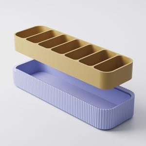 Puede incluir: Un juego de organizadores de dos piezas. La secci&oacute;n superior es de color amarillo mostaza con seis compartimentos rectangulares. La secci&oacute;n inferior es de color p&uacute;rpura claro con detalles de estr&iacute;as verticales. El organizador est&aacute; dise&ntilde;ado para guardar objetos peque&ntilde;os.
