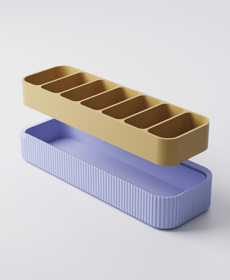 Puede incluir: Un juego de organizadores de dos piezas. La secci&oacute;n superior es de color amarillo mostaza con seis compartimentos rectangulares. La secci&oacute;n inferior es de color p&uacute;rpura claro con detalles de estr&iacute;as verticales. El organizador est&aacute; dise&ntilde;ado para guardar objetos peque&ntilde;os.