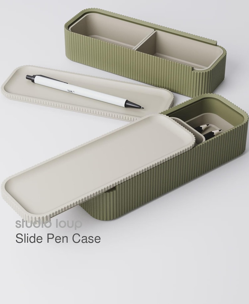 Peut inclure: Trousse &agrave; stylos coulissante vert olive avec int&eacute;rieur et couvercle gris clair. Un stylo blanc avec des d&eacute;tails noirs repose sur un plateau gris clair. Le texte "studio loup Slide Pen Case" est visible.